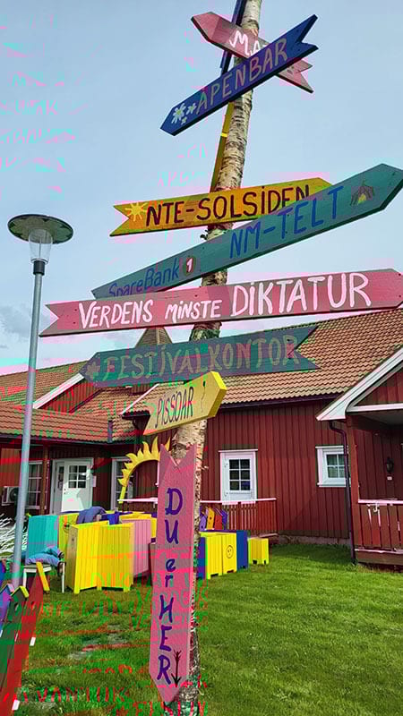 Brightly painted signpost with humorous directions, including "World's Smallest Dictatorship".