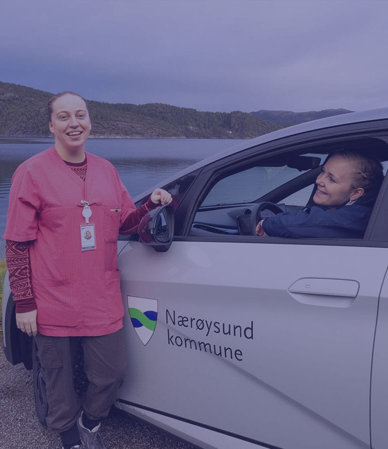 Two women smile by a Nærøysund kommune car near a lake.