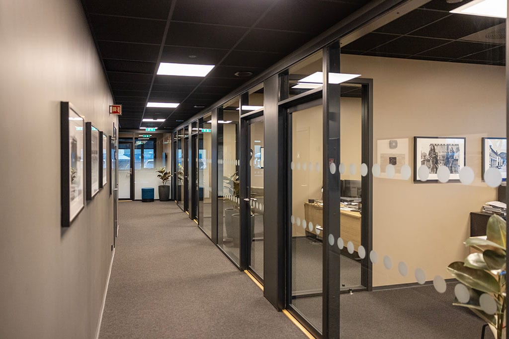 A long office hallway with a black ceiling, gray carpet, and glass-walled rooms featuring frosted dots.