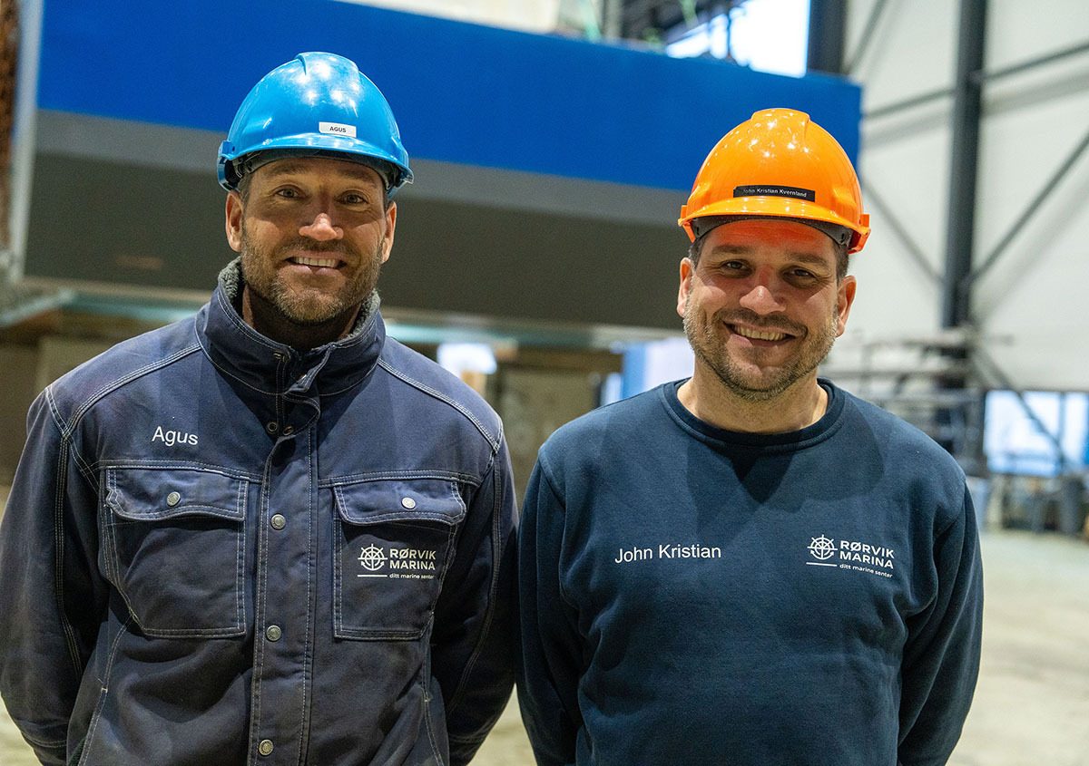 Agus and John Kristian in hard hats and Rorvik Marina workwear, smiling.