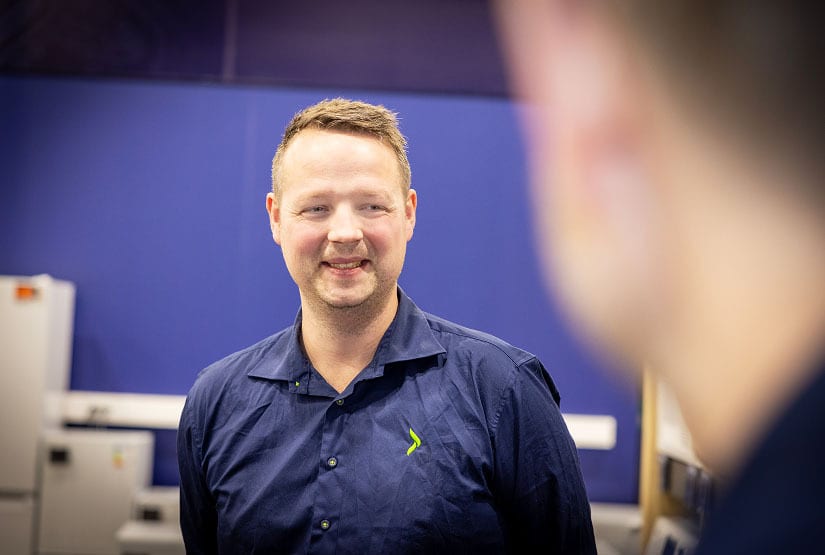 Smiling man in a blue shirt, looking right, with a blurred person in the foreground.