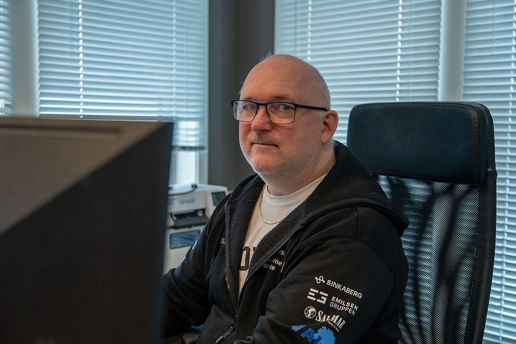 Bald man in glasses and hoodie, smiling, at office desk with computer.