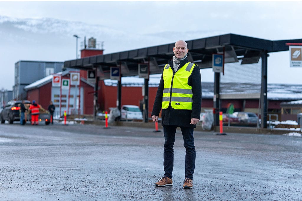 Smiling man in a yellow safety vest at an outdoor recycling facility.