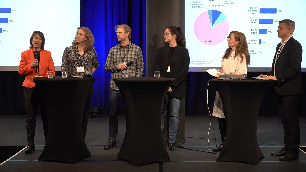 Six people on stage for a panel discussion, with data charts on a screen behind them.