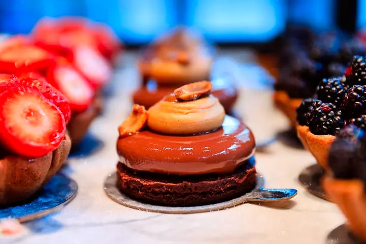 Chocolate glazed dessert in focus, flanked by strawberry and blackberry tarts.
