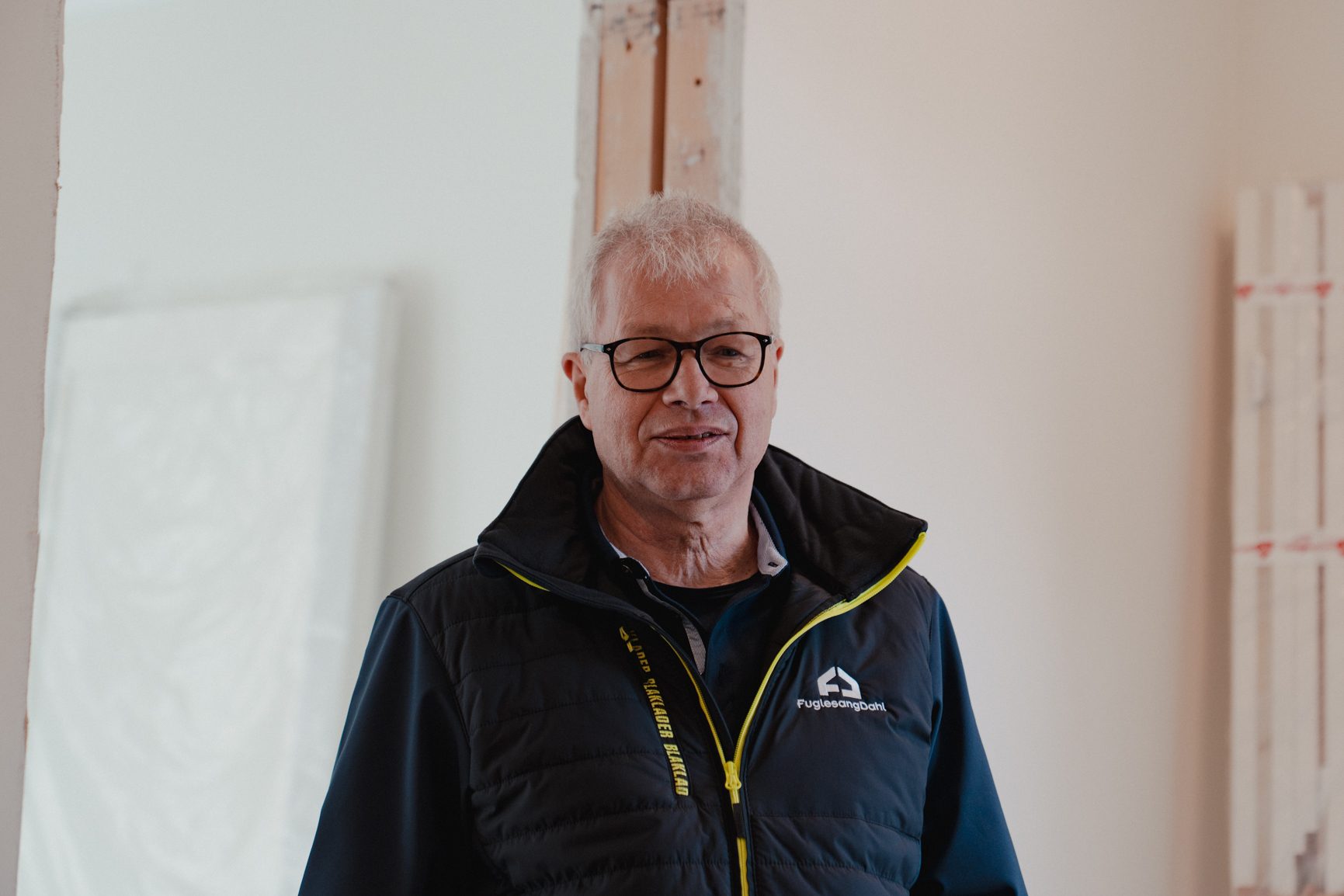 Older man in glasses and a dark vest, smiling.