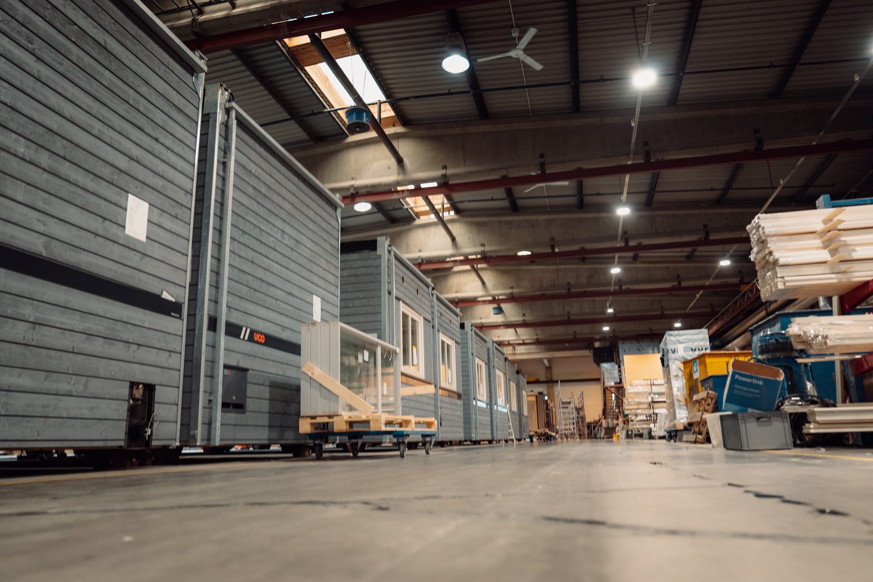 Modular grey building units resembling small homes lined up in a factory.