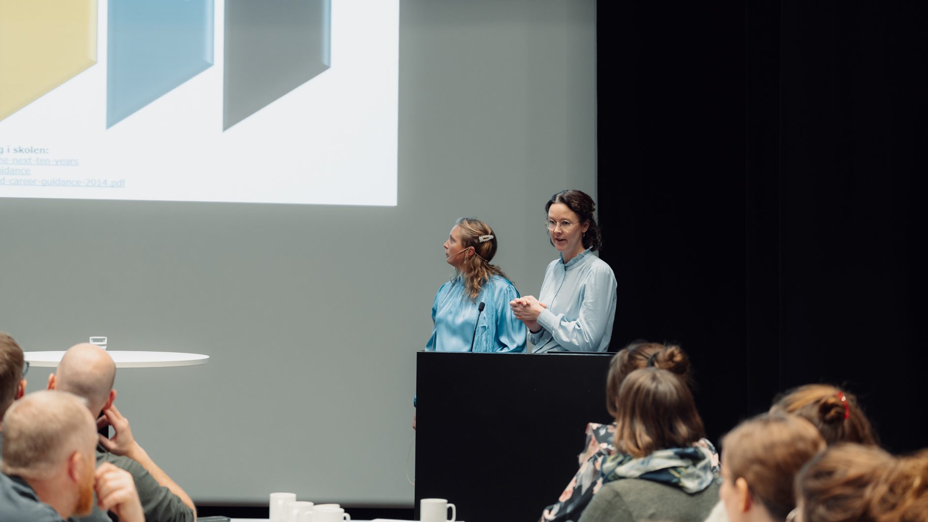 Two women present career guidance on screen to an audience.