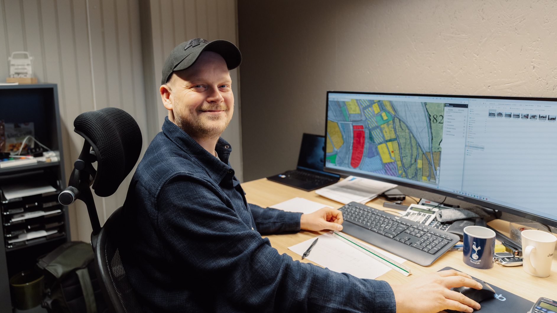 Smiling man at a desk with a computer showing a map, using a mouse.