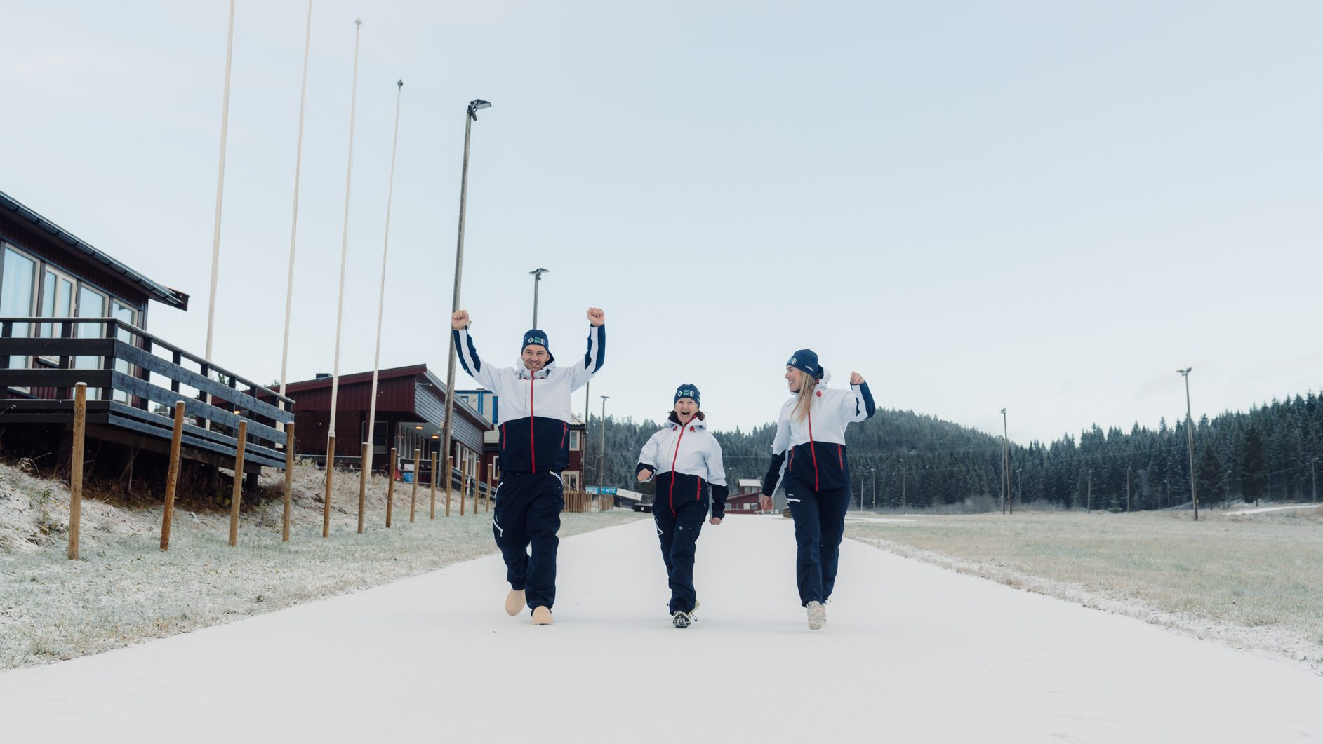 Three people in winter gear celebrate on a snowy road.