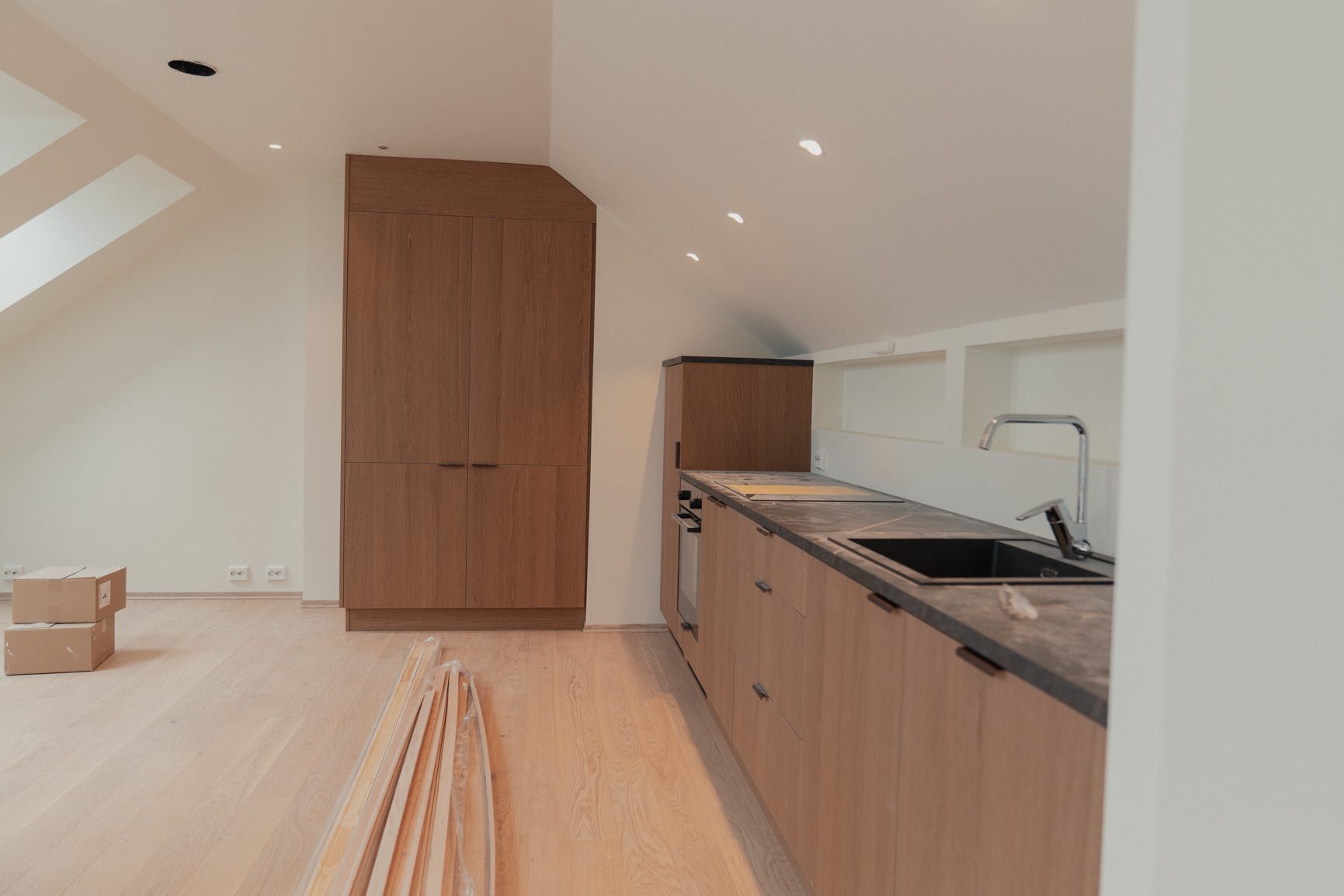 Newly installed kitchen in an attic space with wooden cabinets, dark countertops, and a light wood floor.