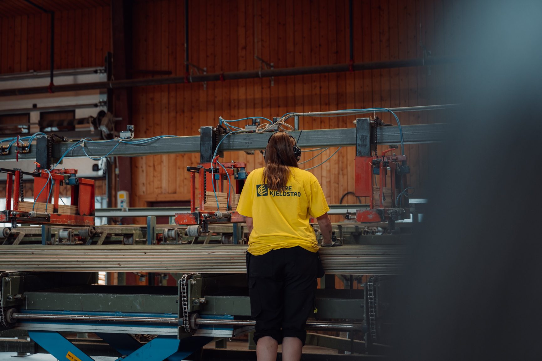 Worker in yellow shirt operates wood processing machinery.