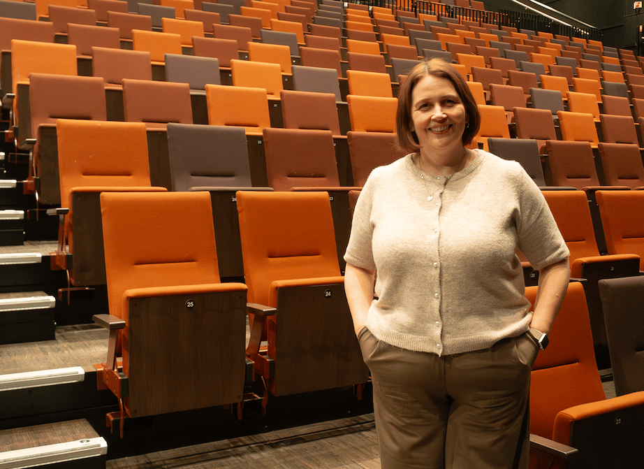 Smiling woman in an auditorium with rows of orange and brown seats.