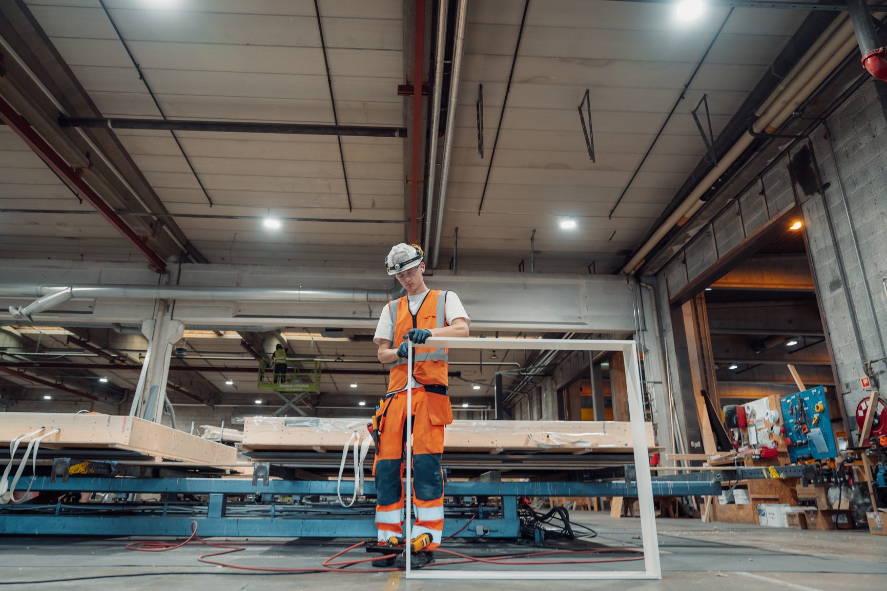 Man in safety gear measures a white frame in a factory.