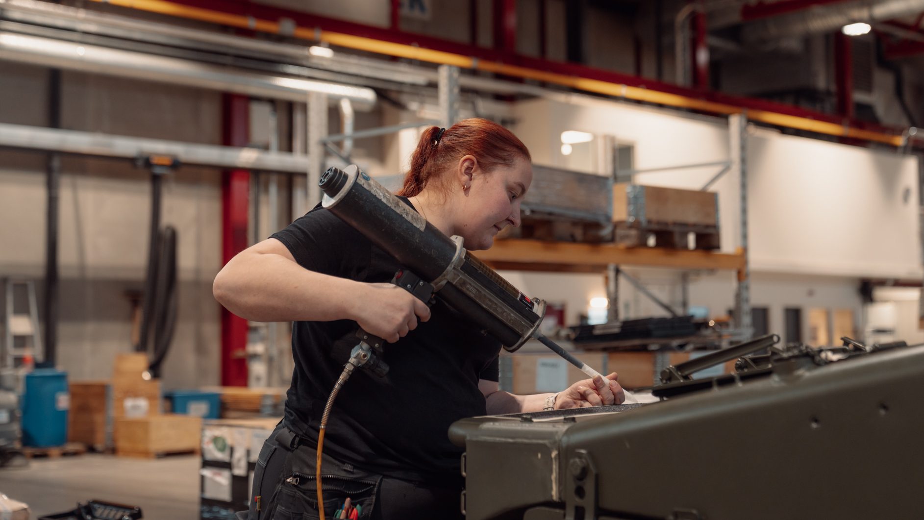 Woman applying sealant to equipment with a pneumatic tool in a workshop.