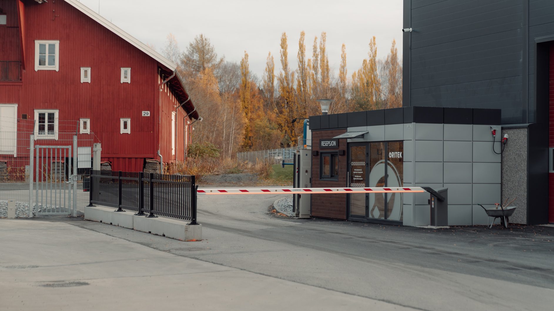 Red building, reception booth with "RESEPSJON" sign, barrier gate, and autumn trees.