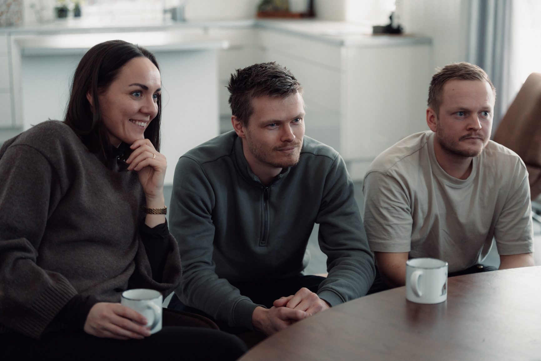 Three people, two men and one woman, seated at a table, attentively looking forward or to the right.