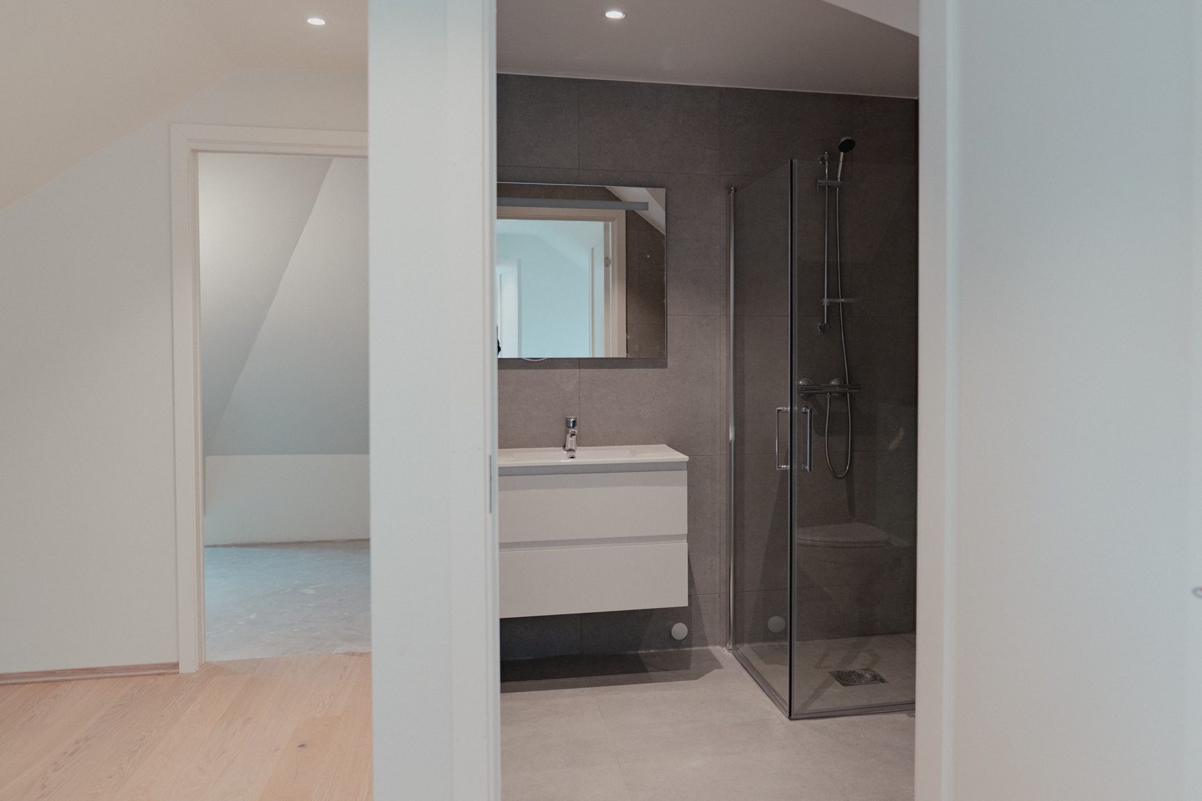 A modern bathroom with a sink, shower stall, and an open doorway to an empty room.