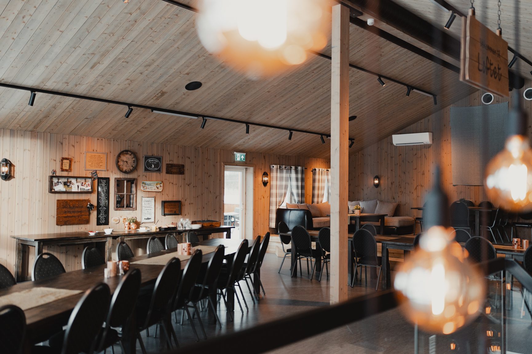 Rustic wooden dining hall with long tables, chairs, and a separate lounge area.