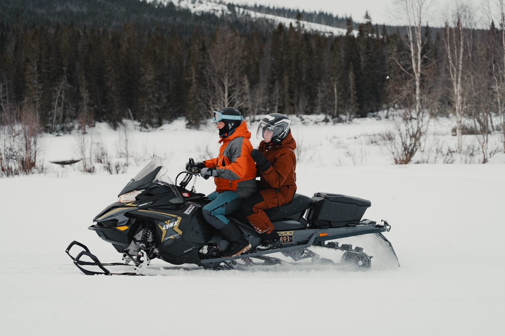Two people on a snowmobile in a snowy forest.