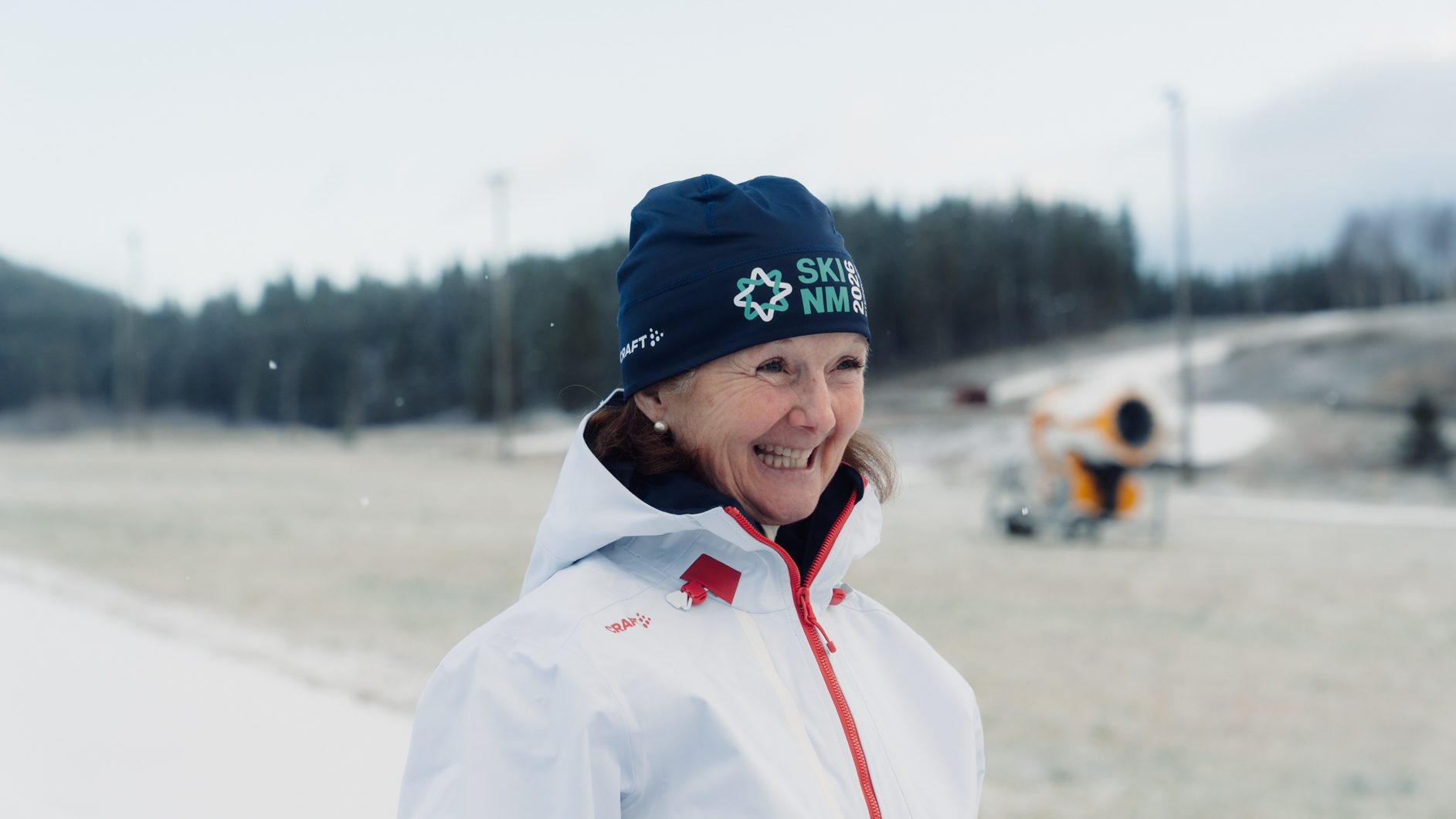 Smiling woman in winter clothes, blue beanie, snowy landscape.