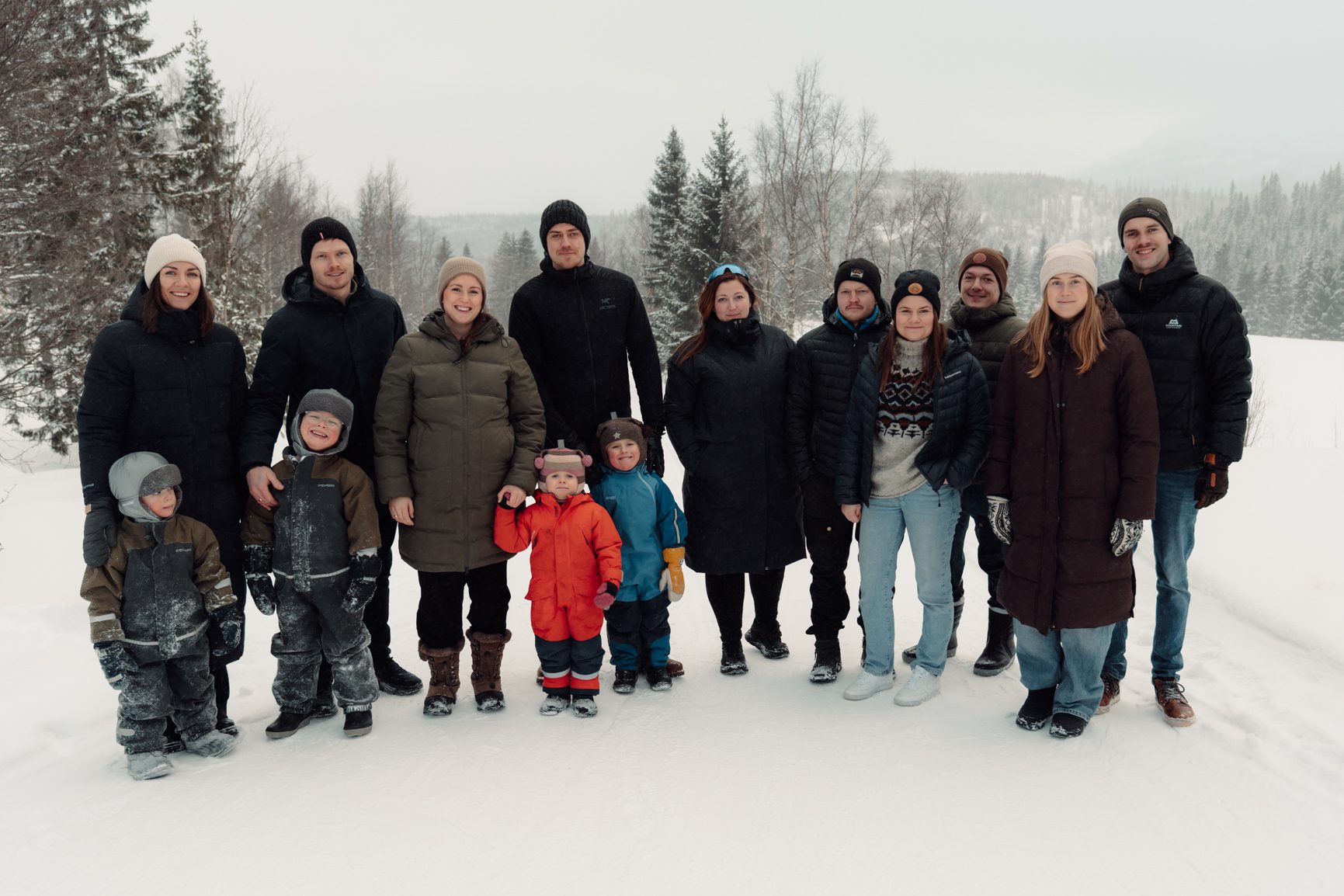 A large family group of adults and children smiling and posing for a picture in a snowy winter landscape.