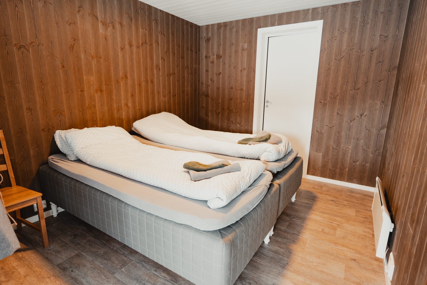 Bedroom with two single beds, wooden paneled walls, and a white door.