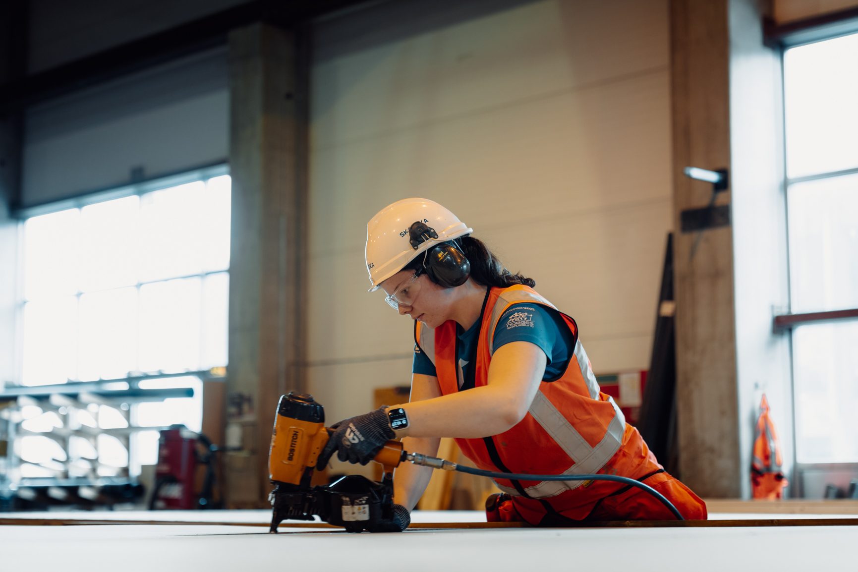 Female worker in PPE operating a nail gun.