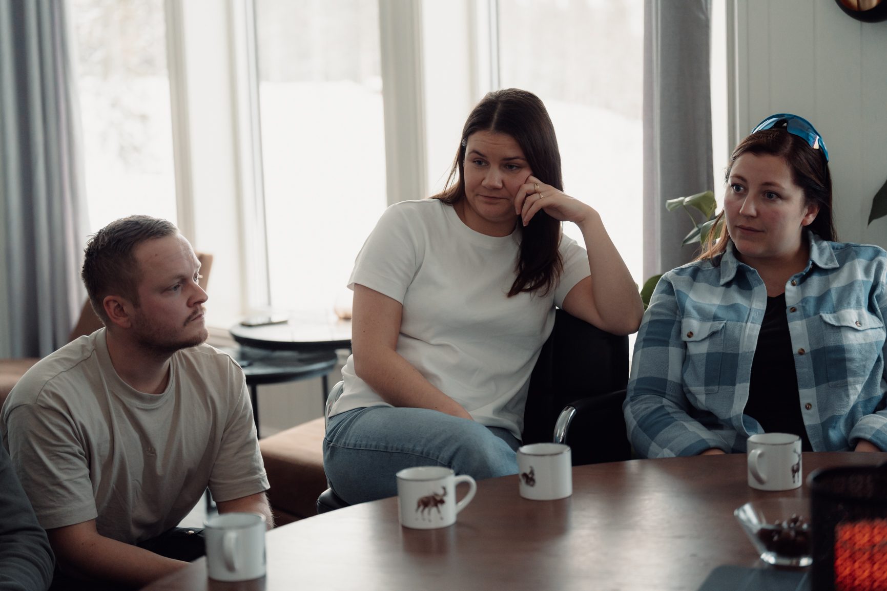 Three people, two women and one man, sitting at a table with coffee mugs, engaged in conversation.
