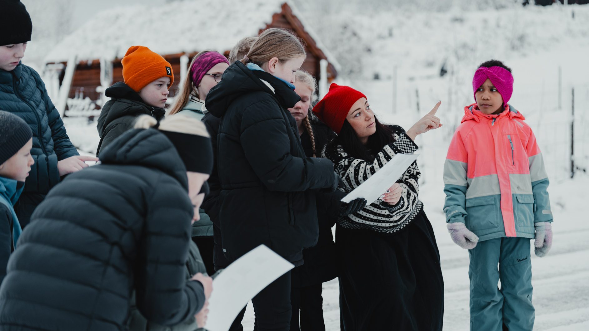 An adult points and explains to a group of children in snowy outdoors.