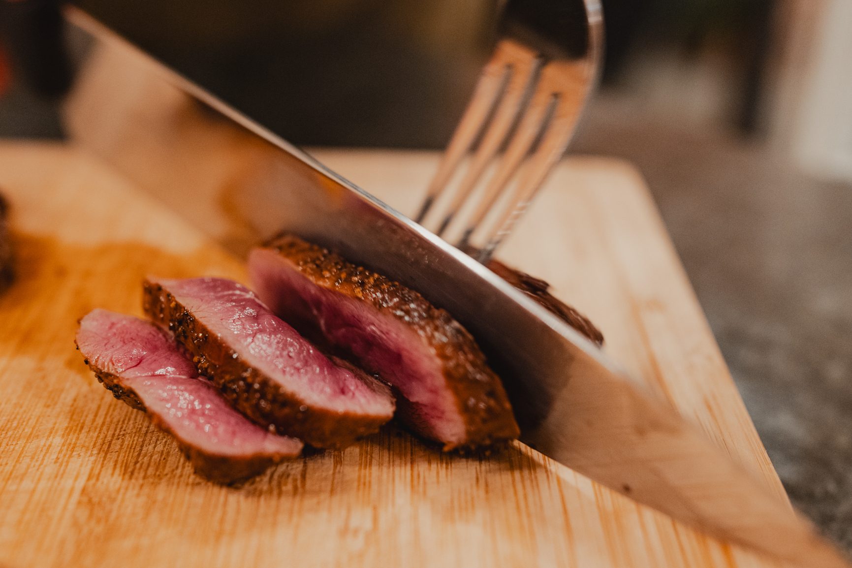 Knife slicing medium-rare meat on a wooden cutting board.