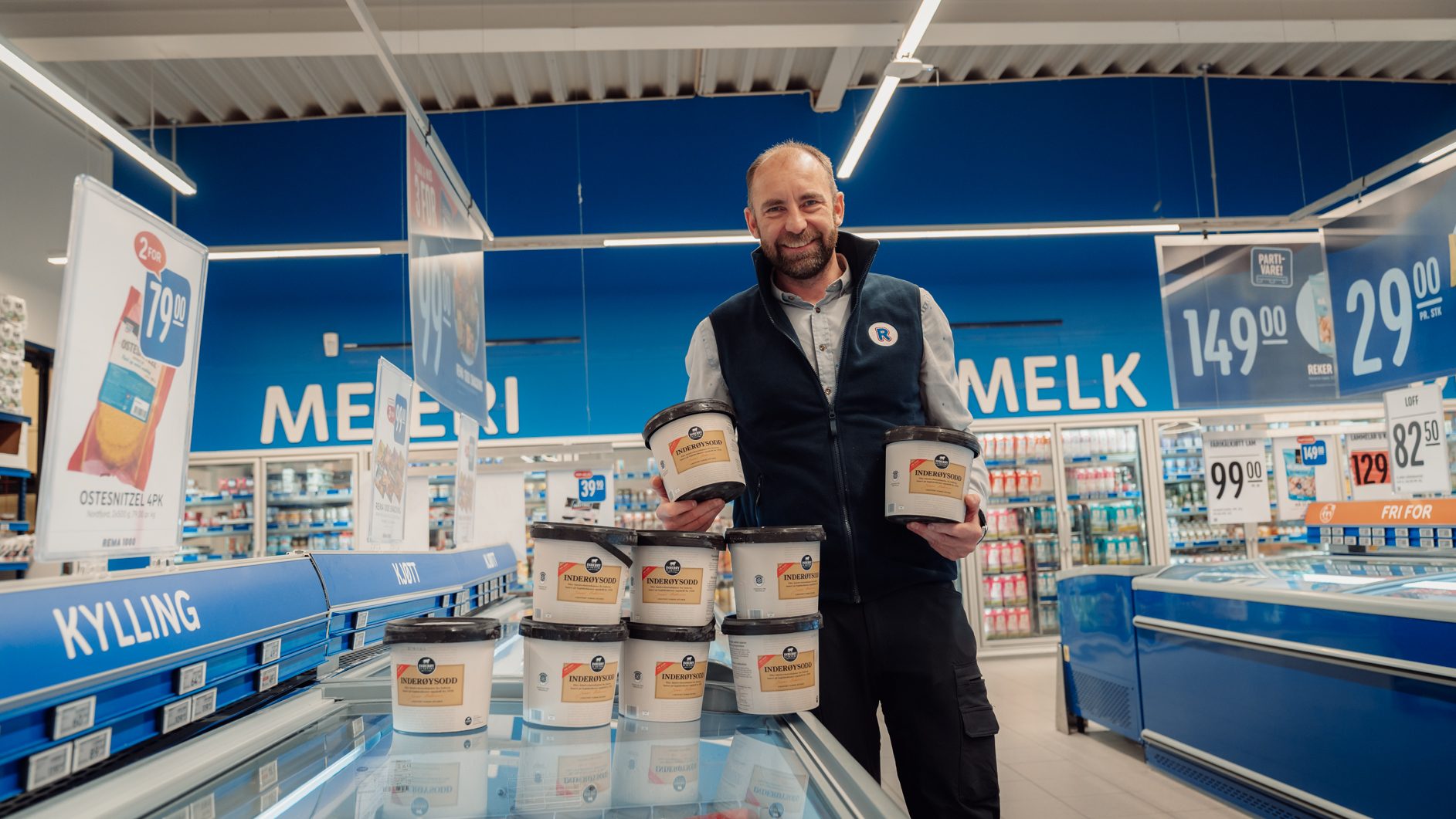 A man holds tubs of "Inderøysodd" in a supermarket aisle.