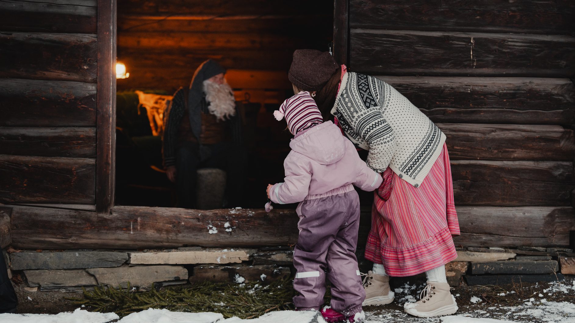 Two kids peek into a rustic cabin at a bearded man, with snow on the ground.