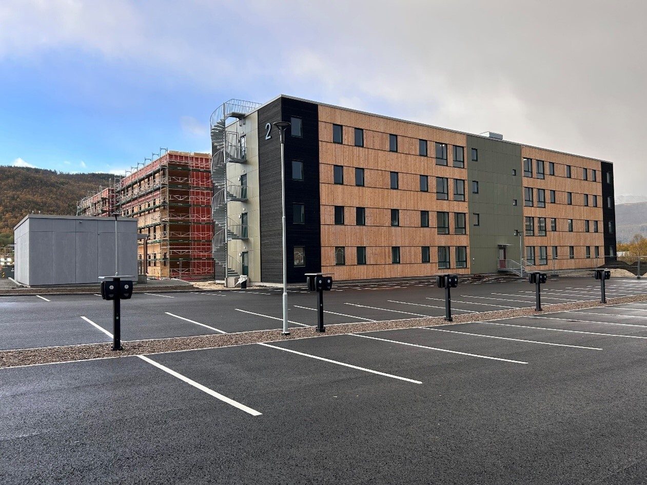 New building with wood siding, construction site, and a parking lot with EV charging stations.