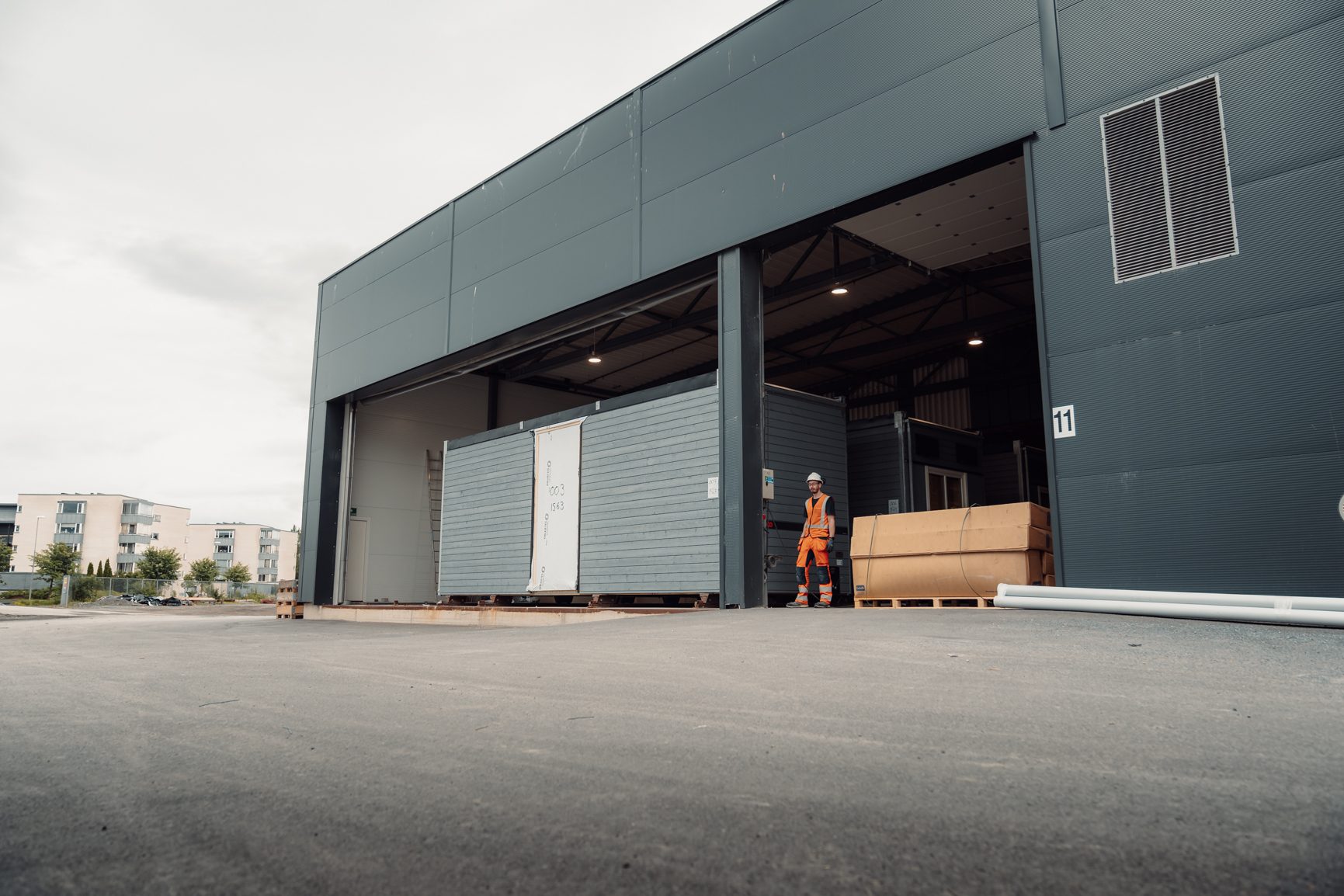 Worker in safety gear stands by a modular building section at a warehouse loading bay.