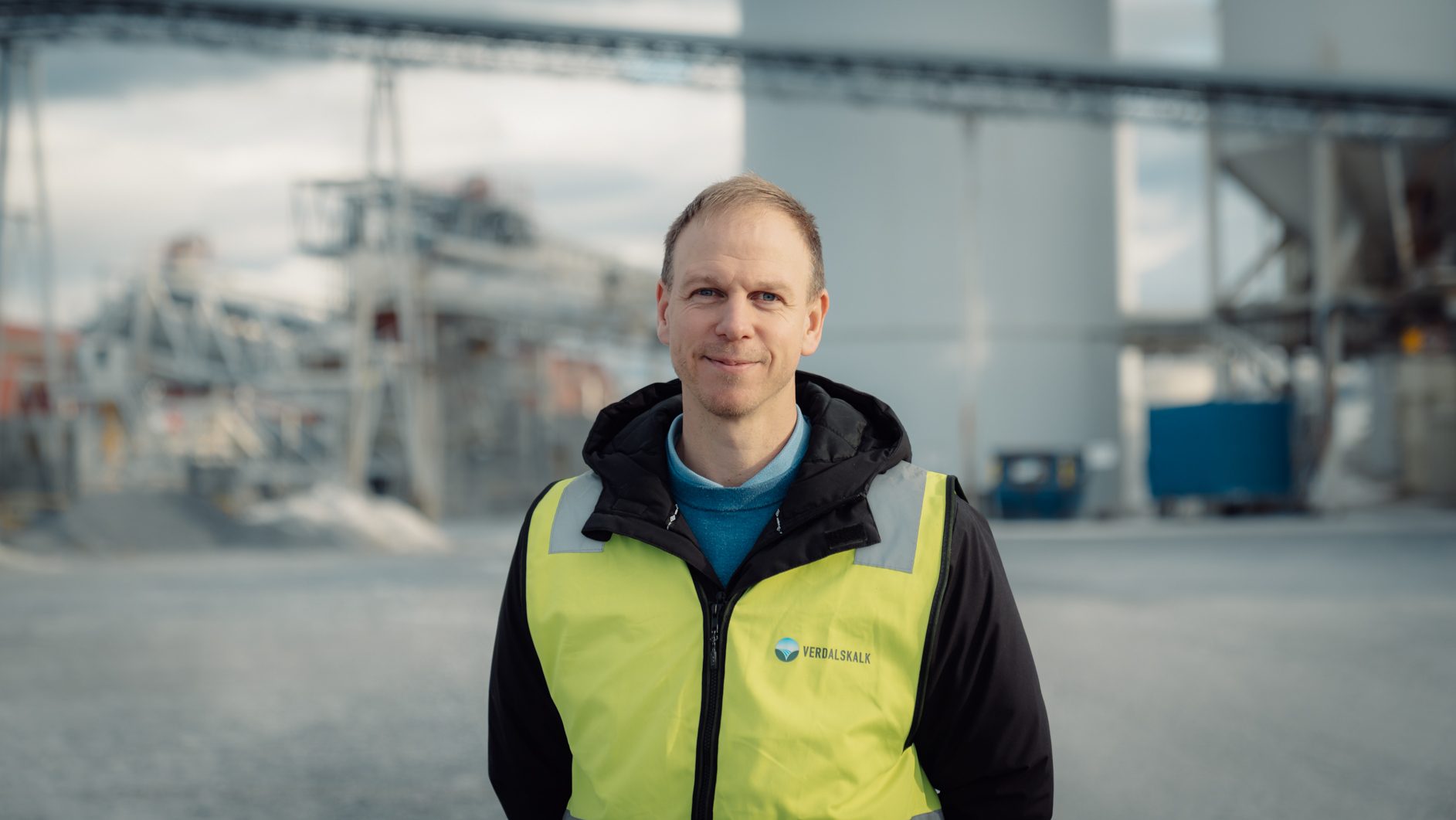 Smiling man in a high-vis vest at an industrial site.