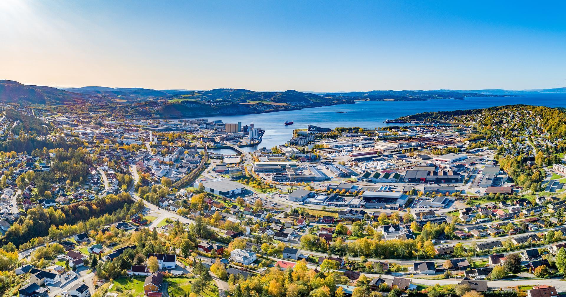 Panoramic aerial view of a town by a blue fjord, surrounded by autumn hills.