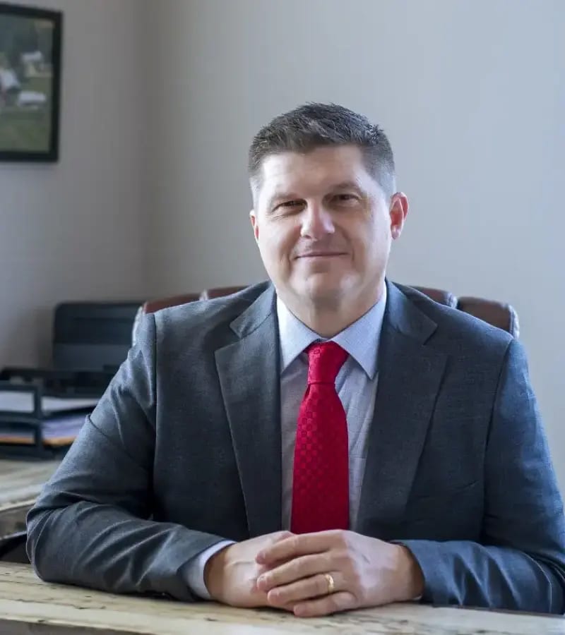 Professional man in a grey suit and red tie, smiling slightly and looking at the camera.