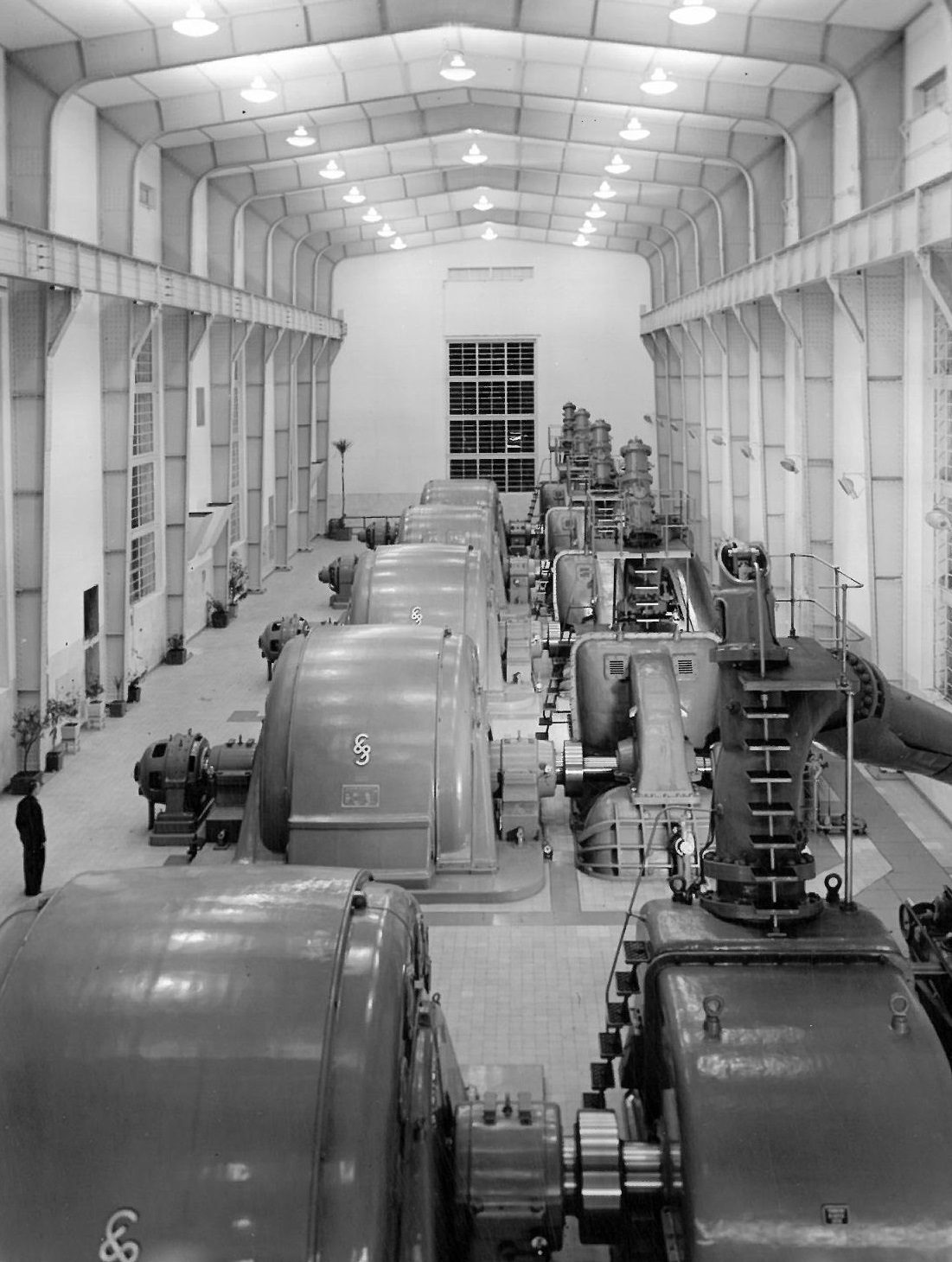 A black and white view of a spacious industrial power plant hall with rows of large generators.
