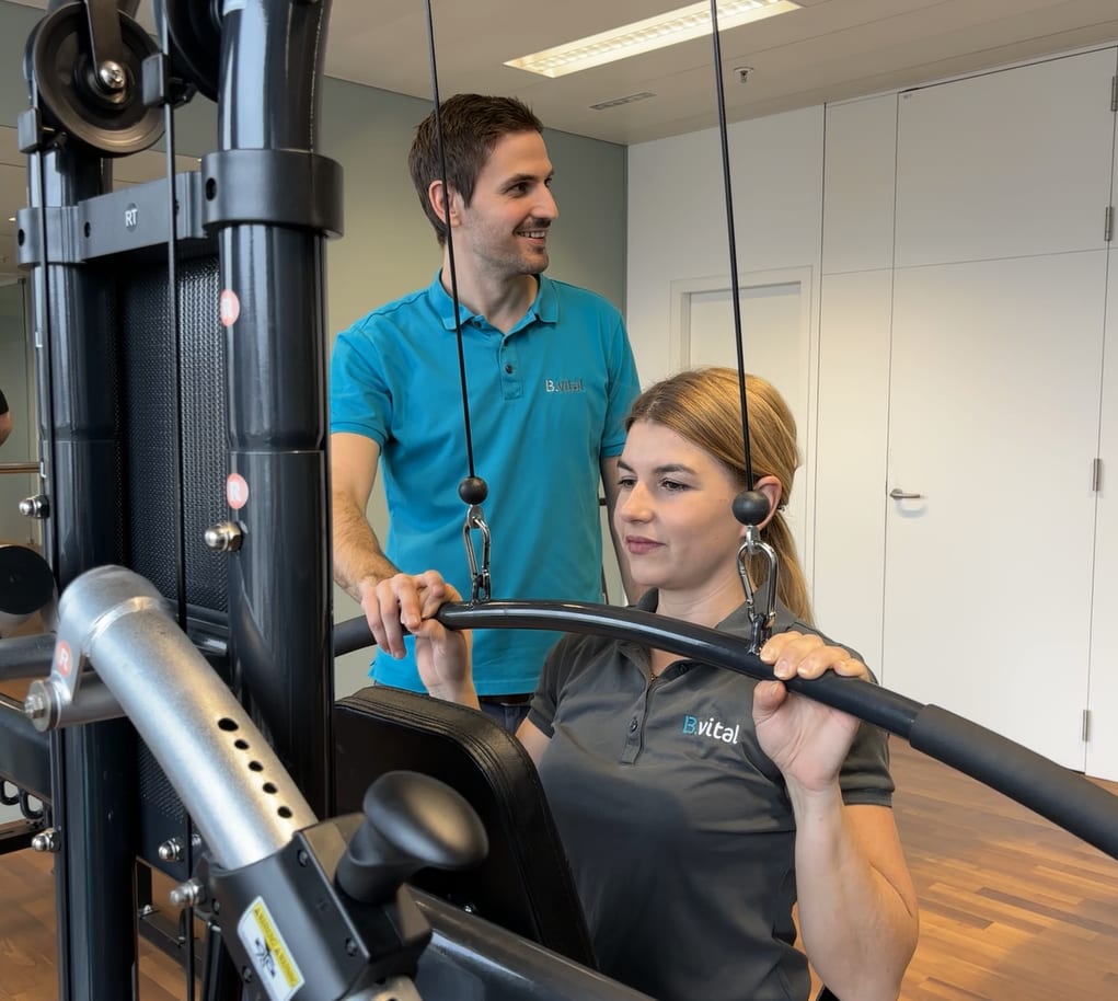 Trainer guiding woman on a gym machine during a B.vital workout.