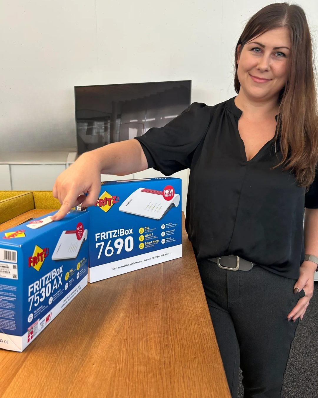 Smiling woman points at two FRITZ!Box routers, including the 7690 with new Wi-Fi 7.