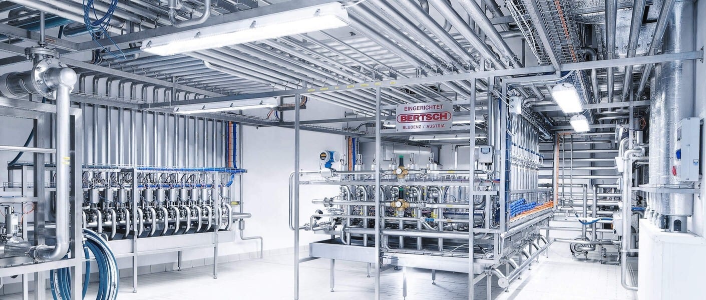 Bright, clean industrial facility with extensive stainless steel pipes and processing equipment. BERTSCH sign.