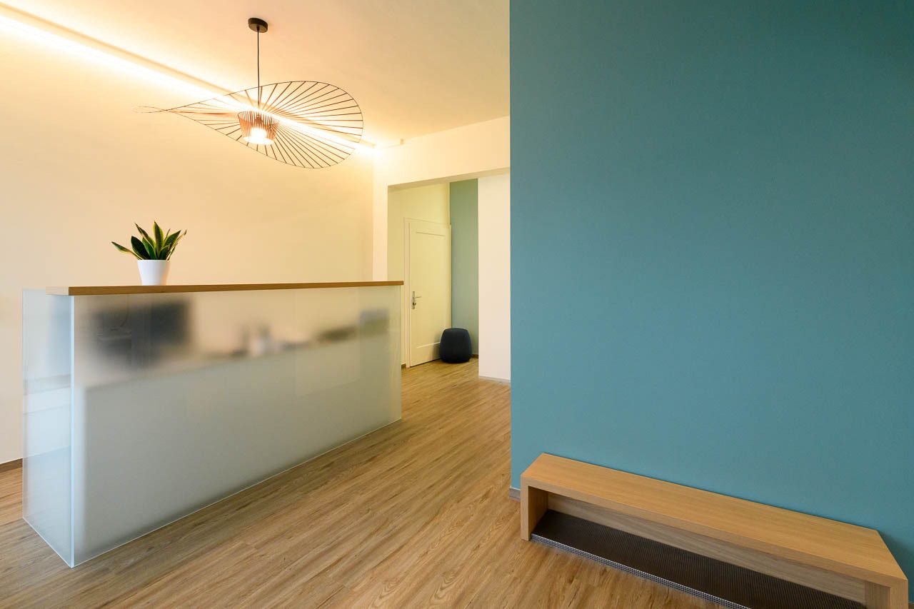 Modern reception area with frosted glass desk, wooden floor, teal wall, and unique lamp.