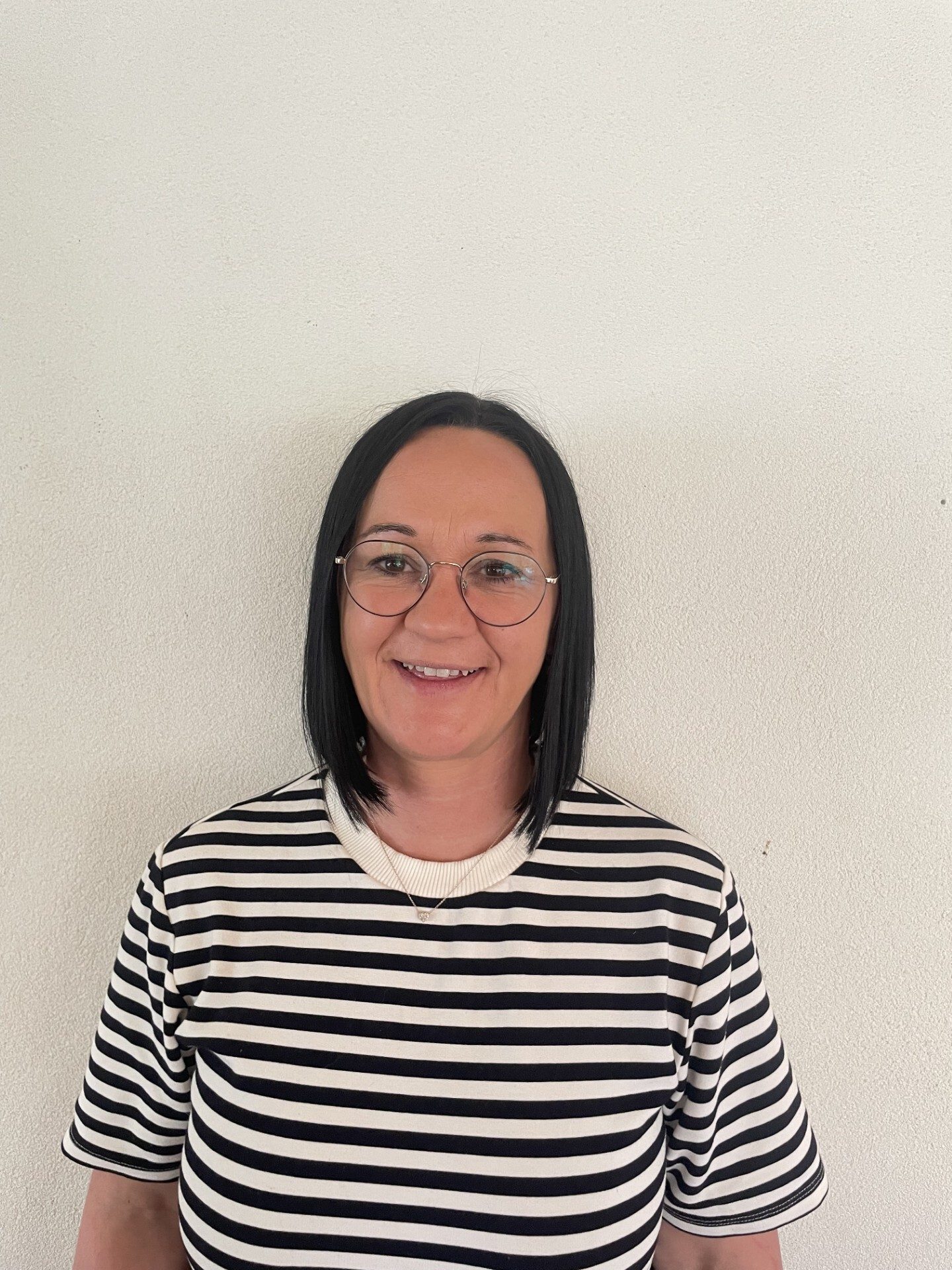 Smiling woman with black hair, glasses, and a striped shirt on a white background.