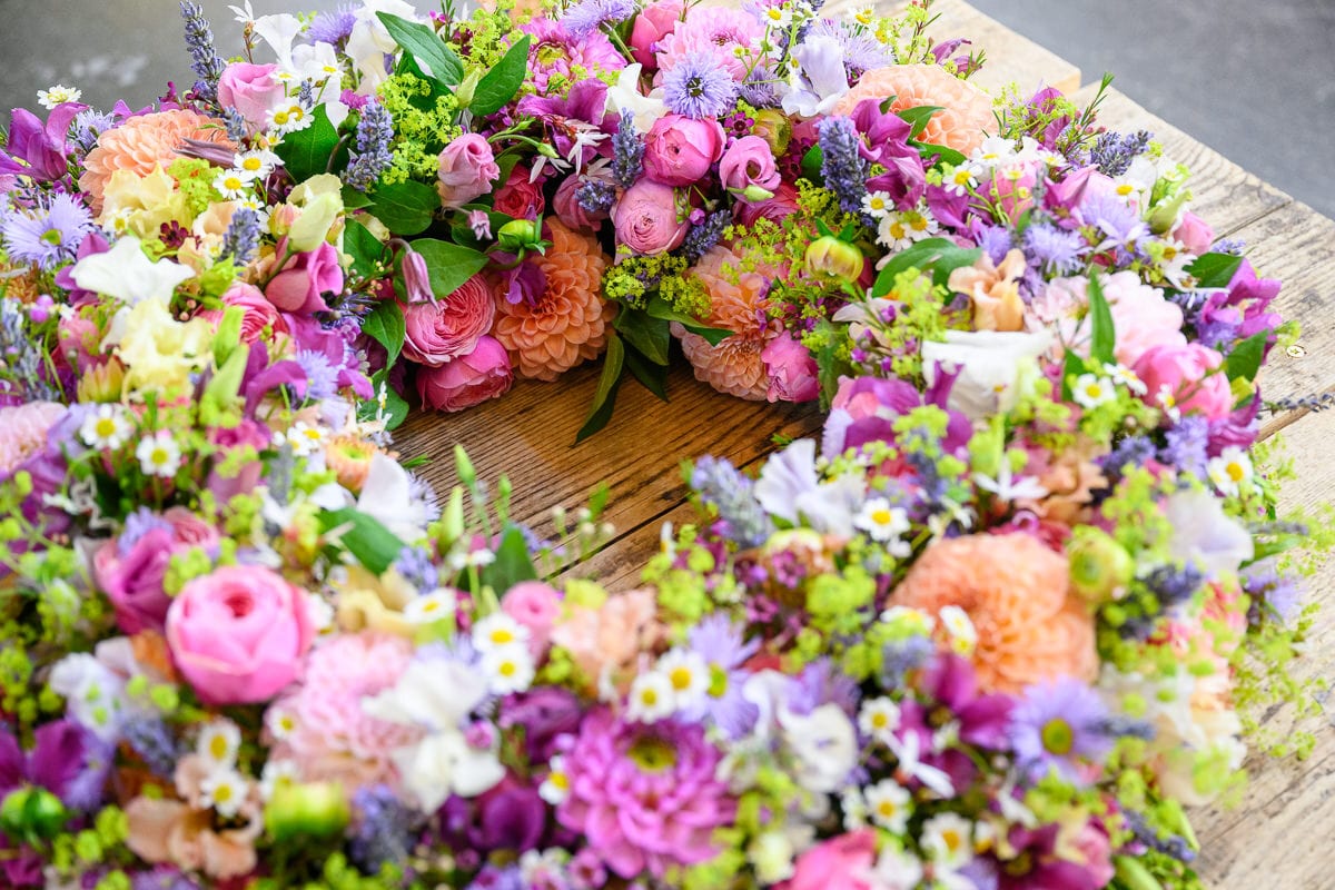 A vibrant, colorful floral wreath composed of various blossoms, resting on a rustic wooden surface.