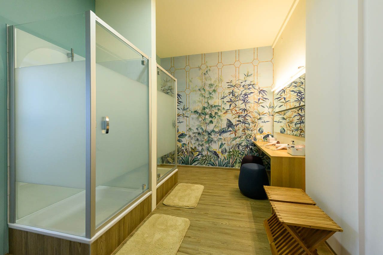 Vibrant bathroom with frosted shower, tropical wallpaper, wooden vanity, and floor.