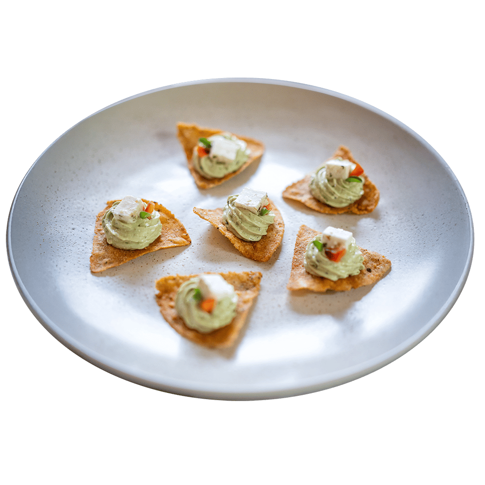 Appetizer plate: six triangular chips with green avocado dip, feta, red peppers.