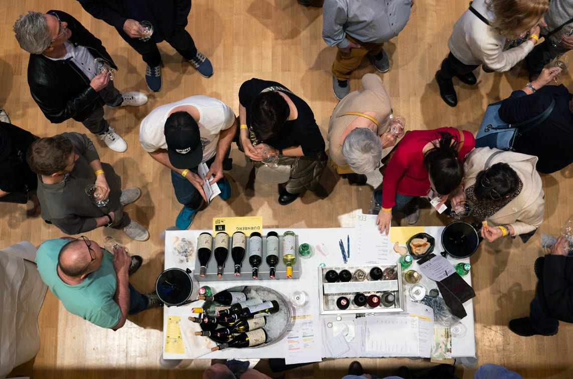 Overhead view of people gathered around a table, tasting wine and looking at bottles.