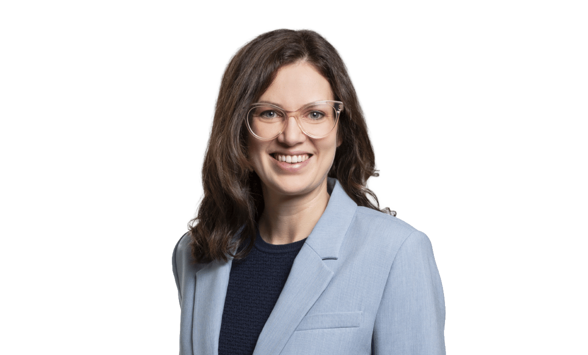 Smiling professional woman with glasses and wavy brown hair wearing a light blue blazer.