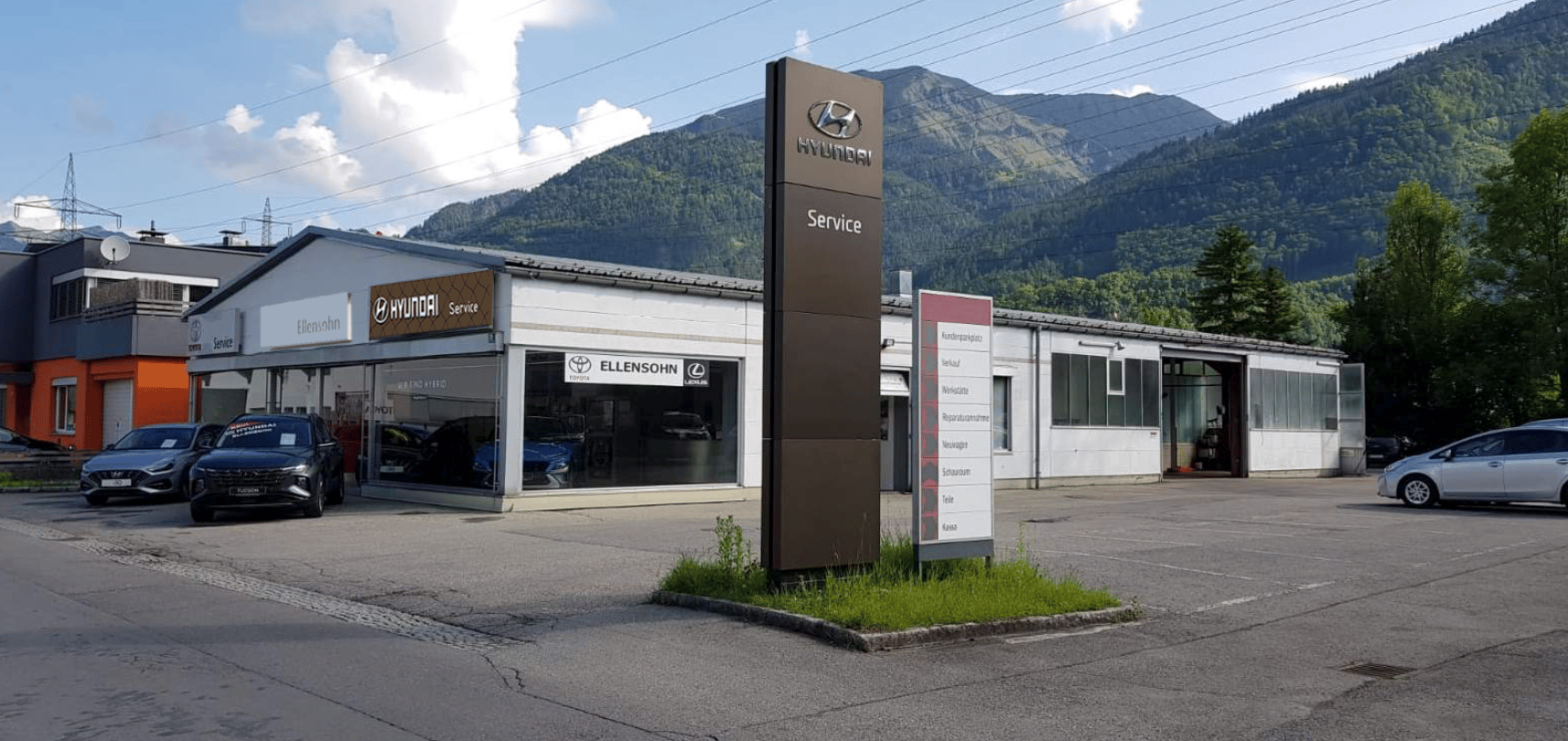 A Hyundai and Ellensohn car dealership with cars for sale in the foreground, against a backdrop of mountains.